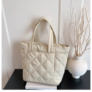 Detail of quilted beige tote bag showing rhombic stitching and large front pocket