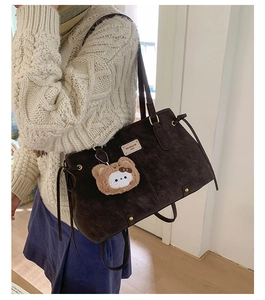 Detail of dark brown suede tote bag with drawstring knots and plush bear charm accessory