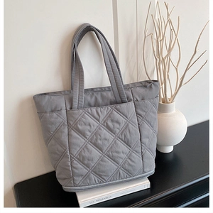 Detailed view of gray quilted tote bag with diamond pattern displayed on bookshelves