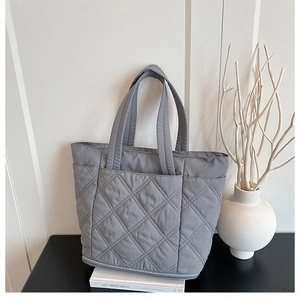 Detailed close-up of grey quilted tote bag with diamond stitching on a modern table