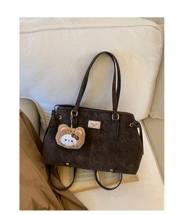 Detail of vintage brown suede shoulder bag with plush bear charm on a beige sofa