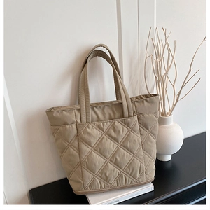 Detail of quilted khaki tote bag with wide handles and front pocket in a minimalist setting