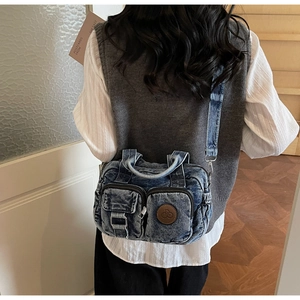Detailed view of a vintage wash denim crossbody bag with dual zipper pockets and leather tag