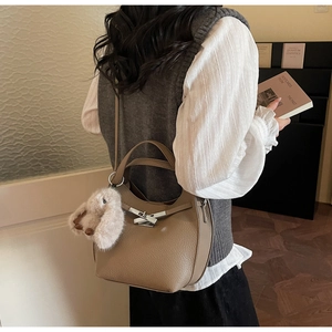 Brown lychee leather bucket bag detail with metal lock and plush bunny charm on model