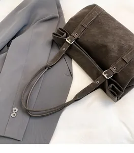 Detail of dark brown suede shoulder bag with adjustable silver buckles on grey suit