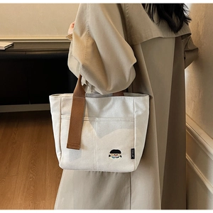 Détail d'un cabas en toile blanc cassé avec broderie élégante et anses de couleur marron