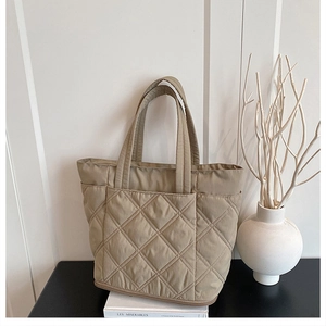 Detailed view of khaki quilted tote bag on white books with minimalist home decor