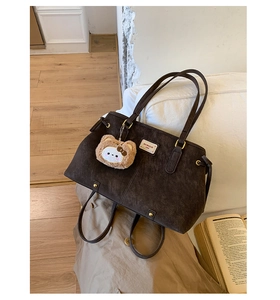 Detail of dark coffee suede tote bag with metal rivets and fluffy bear charm accessory