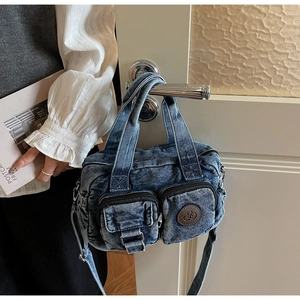 Detail of vintage blue denim crossbody bag featuring dual front pockets and leather logo