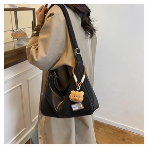 Detail view of black crescent shoulder bag with a brown teddy bear charm and fashion label