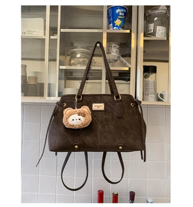 Detailed close-up of dark brown suede tote bag with branding and cute cat plush charm