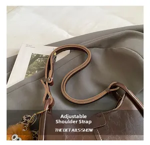 Dettaglio della tracolla regolabile su una borsa a secchiello in pelle marrone con ciondolo