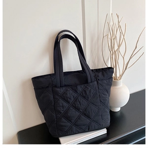 Macro detail of black quilted tote bag with diamond stitching on a minimalist table