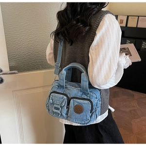 Detail of blue denim crossbody bag featuring multiple functional pockets and wide strap
