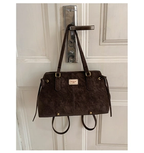 Detail of dark brown vintage faux leather shoulder bag with gold metal logo and side drawstring