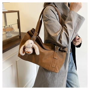 Detail view of large brown suede tote bag with cute plush bunny charm and shoulder strap