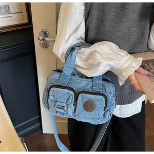 Detailed view of the blue denim crossbody bag featuring dual front pockets and top handle
