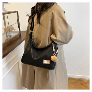 Detail of black faux leather tote bag with plush bear charm and fashion label tag