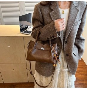 Detail of vintage brown leather crossbody bag with wooden bead tassel and metal lock
