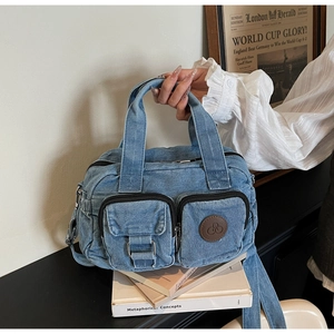 Detail of vintage blue denim crossbody bag with dual utility pockets and brown logo patch