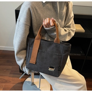 Detail of grey canvas tote bag with brown handles and cute embroidered character patch