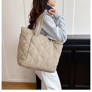 Detail of a large beige quilted tote bag with diamond stitching shown on a shoulder
