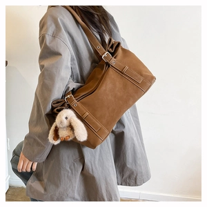 Macro detail of brown frosted shoulder bag featuring decorative straps and plush rabbit charm