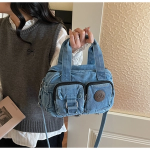 Detailed view of blue denim crossbody bag with dual front pockets and logo detail