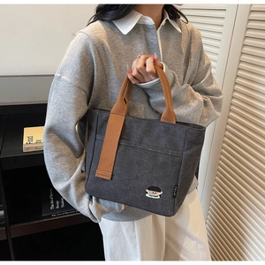 Détail d'un sac cabas en toile grise avec anses marron et broderie délicate