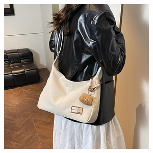 Detail of white leather tote bag with a fashion tag and cute brown plush bear charm