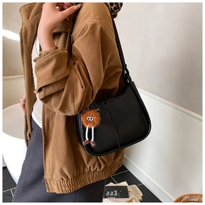 Detail einer schwarzen Hobo-Tasche mit braunem Plüsch-Anhänger an einem Model