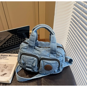 Detail of light blue denim crossbody bag with multiple zip pockets and circular leather logo