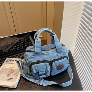 Close-up of washed denim crossbody bag featuring dual front zipper pockets and leather logo
