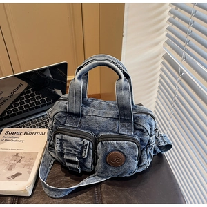 Detailed close-up of blue denim crossbody bag featuring dual front zipper pockets