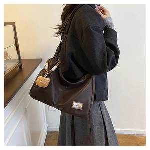 Detailed view of brown tote bag featuring plush bear charm and fashion logo tag