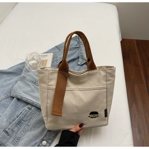 Detail of beige canvas tote bag with cartoon embroidery and brown straps on art magazine