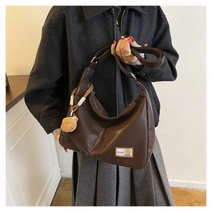 Detail of dark brown leather hobo bag featuring a fashion tag and teddy bear charm