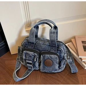 Detailed view of blue denim crossbody bag with dual front pockets and brown leather logo tag