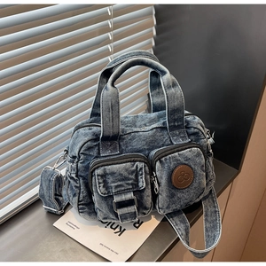 Macro detail of washed denim bag featuring brown leather logo patch and pocket stitching