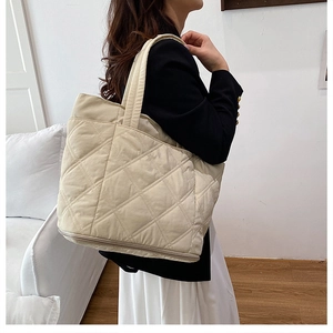 Detail of beige quilted tote bag showing expandable bottom zipper and soft fabric texture