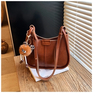 Detailansicht der braunen Leder-Eimertasche mit Plüsch-Anhänger und Logo auf Holzoberfläche