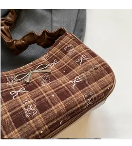 Detail of checkered shoulder bag featuring bear embroidery and ruffled strap handle