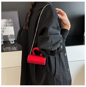 Détail d'un mini sac cylindrique rouge avec chaîne dorée sur un manteau noir chic