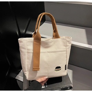 Detailed shot of an off-white canvas tote bag with brown straps and cute girl embroidery