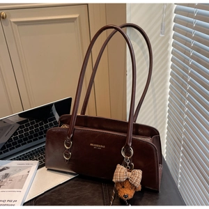Detalle de bolso bajo el brazo retro marrón oscuro con logo dorado y oso de peluche
