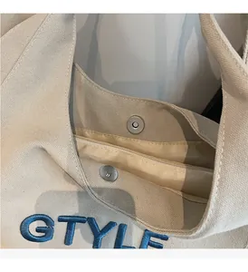 Detail of canvas tote featuring blue G STYLE embroidery and magnetic snap closure