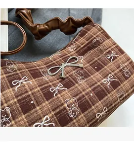 Close-up of brown checkered shoulder bag featuring bear prints and silver bow buckle