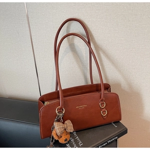 Detalle de bolso retro marrón de hombro con logo dorado y colgante de oso de peluche