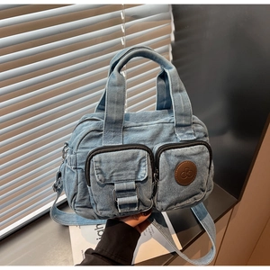 Detail view of blue denim crossbody bag featuring dual front zippers and brown leather patch