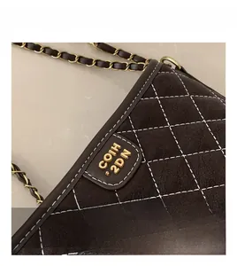 Detail of dark brown quilted suede bag with contrast stitching and golden chain strap
